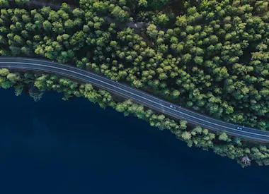 Cars on a two lane road cutting through forest near a body of water