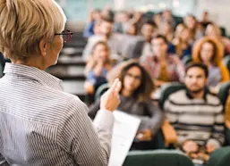 Teacher stands at front of lecture talking to a group of students