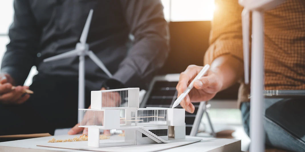 Photo depicting two Two engineering design professionals talking about installing solar panels on the roof of a model house. (© istock.com/sorn340)