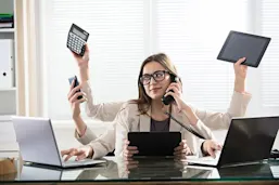 Woman with 8 arms at a desk holding various devices 