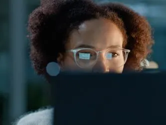 Woman working at a computer, with the monitor screen reflecting in her glasses