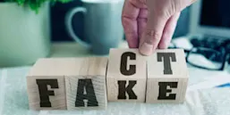 Building blocks with the words fake and fact sit on a desk covered with newspaper.