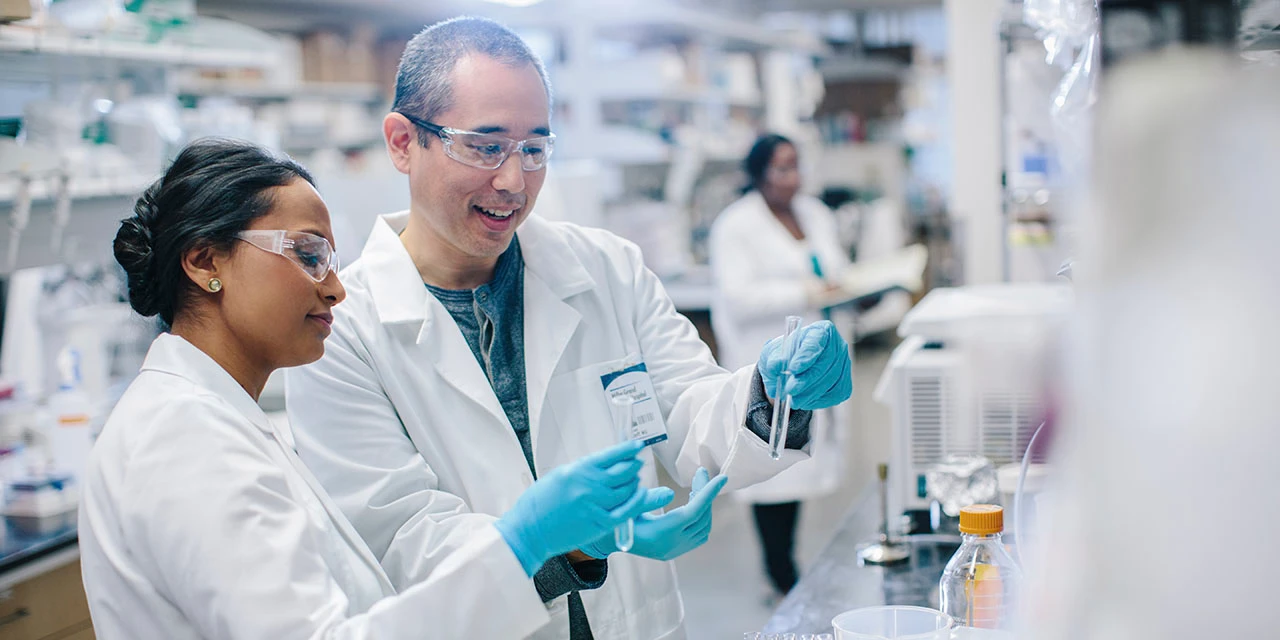 Doctors examining test tubes while coworker working in background at laboratory (Cavan Images/Cavan via Getty Images)