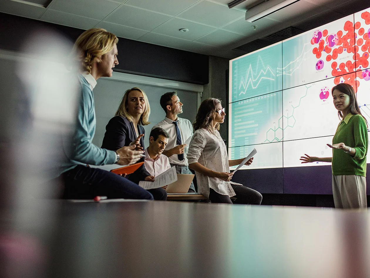 A woman presenting chemistry findings to colleagues in front of a screen.