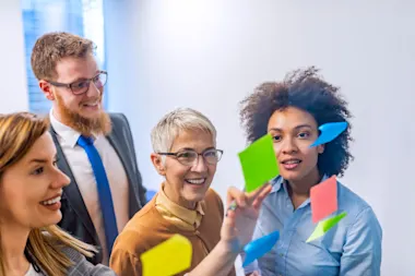 Business people standing in front of glass wall with post-it notes and discussing