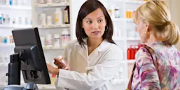 A pharmacist interacts with a patient in front of a computer