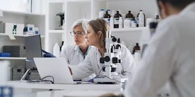 Photo depicting two women and a man working in a pharmaceutical laboratory (DMP/E+ via Getty Images)
