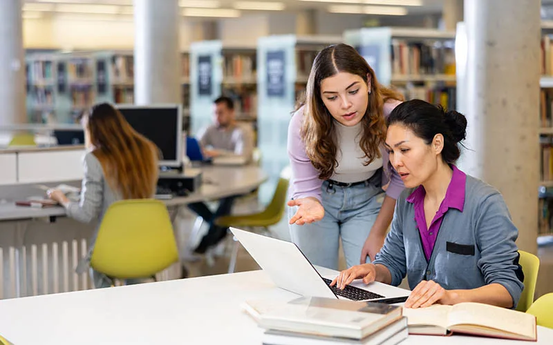 Photo of two college students collaborating in a library (© istock.com/JackF)