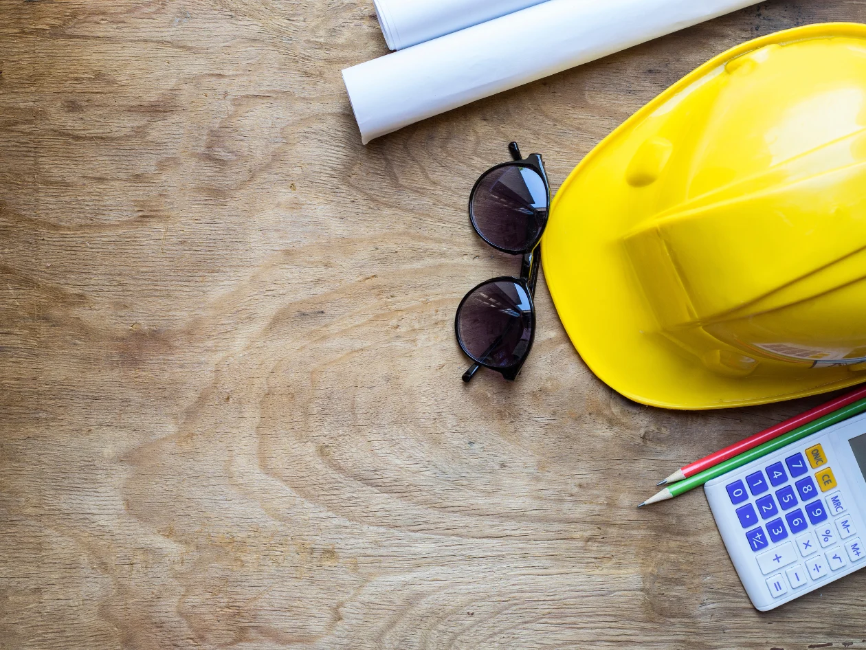 Protection hat, glasses a calculator and papers on top of a table