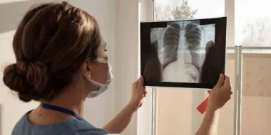 A woman clinician with dark hair is holding an x-ray up to read it.