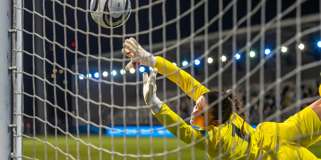 A female goalkeeper diving mid-air to save goal during a match (© istock.com/simonkr)