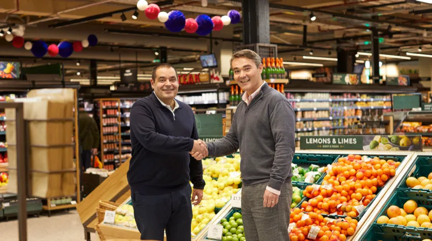 Two men shaking hands in M&S in front of the fruit and veg section. 