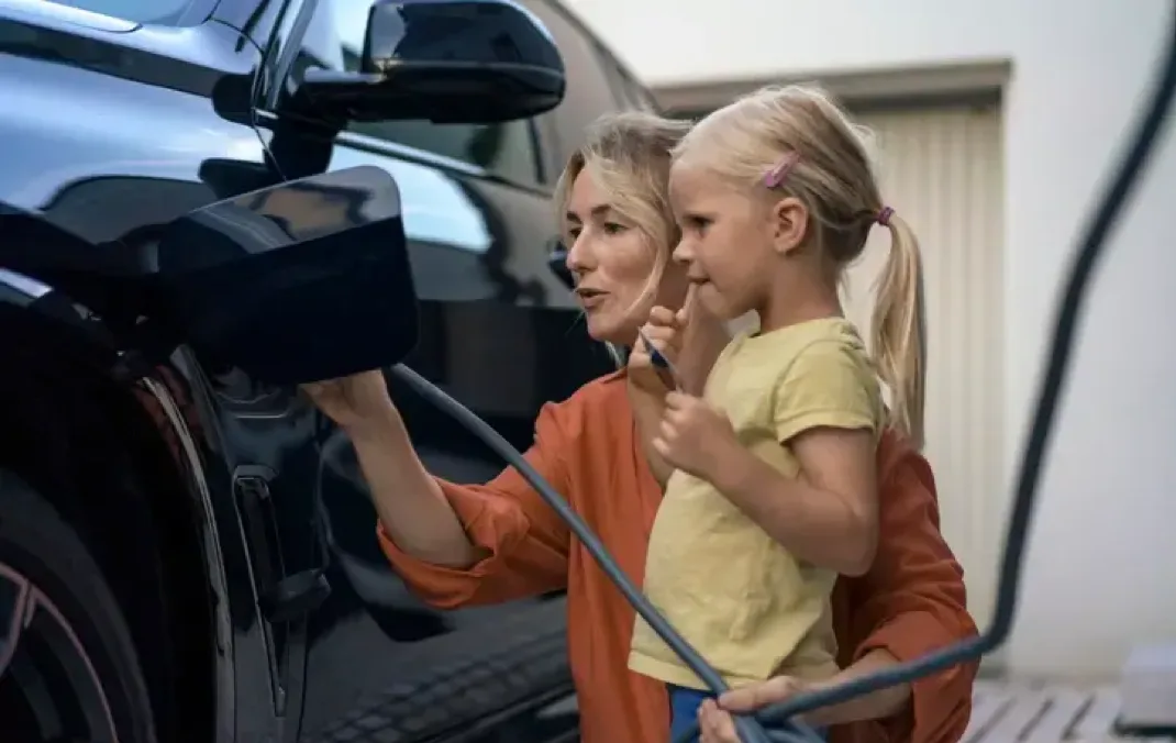 A mother kneeling down next to her daughter, plugging a charging cable into her black Electric Vehicle.