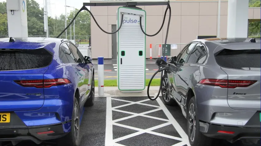 Two vehicles are parked in charging bays infront of a bp pulse 150kw charger. Both cars are plugged in and being charged, one car is blue and the other is silver.