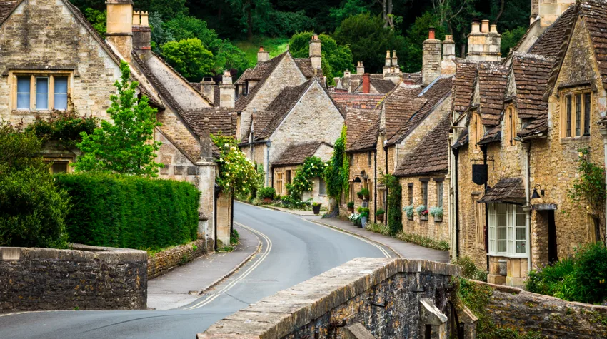 Honey-coloured village homes of the Cotswolds in England are surrounded by greenery all around.