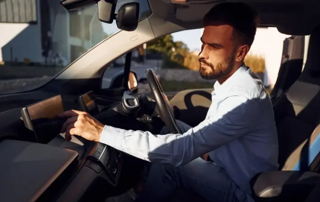 Man sitting in the driver seat of an EV, entering a destination into the Sat Nav.
