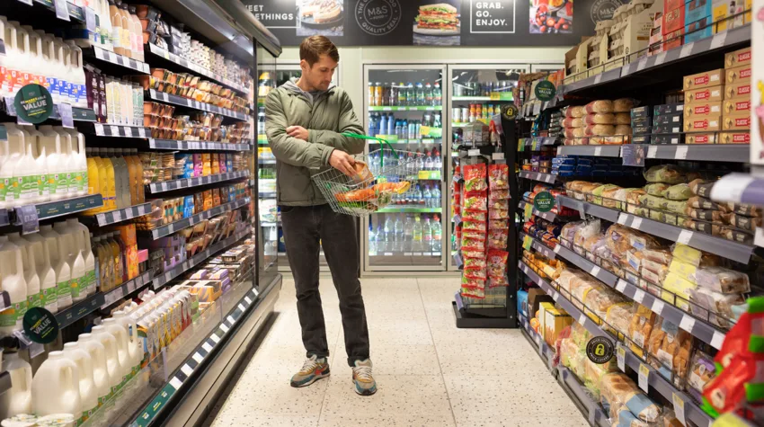 A man putting food in his basket, in an M&S aisle. 