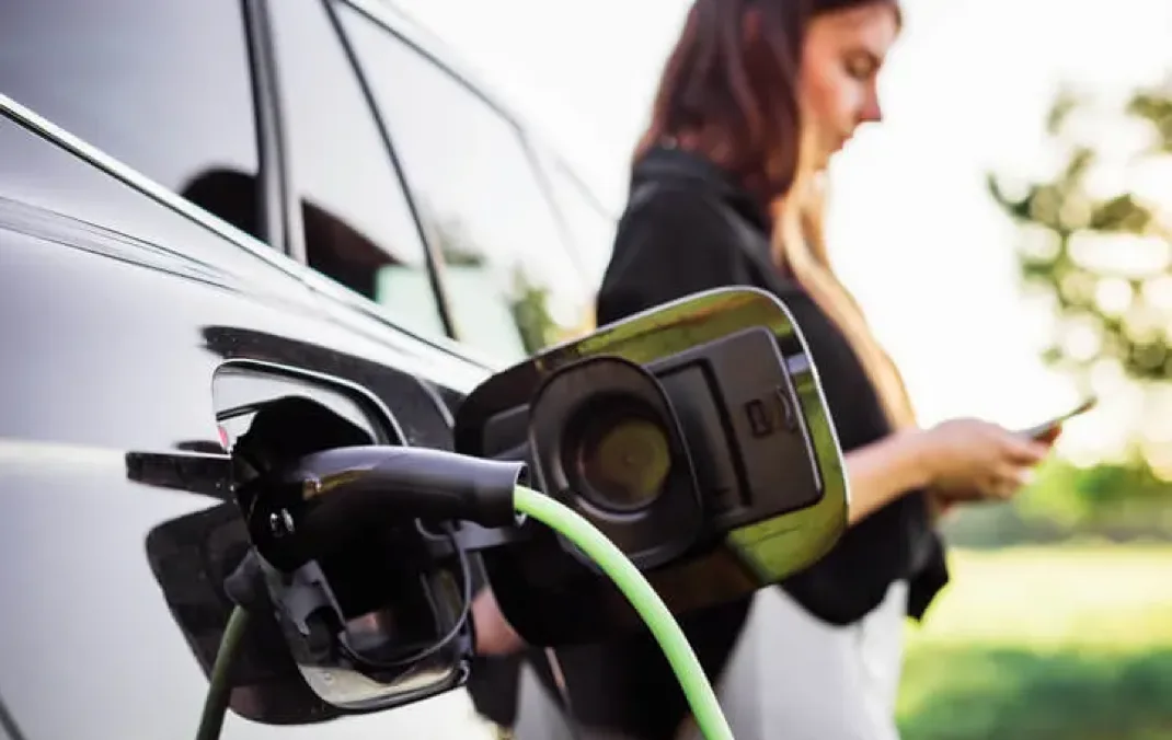 A woman browsing her phone while her electric car is being charged
