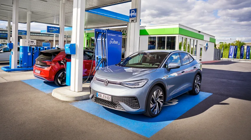 A silver EV at a bp pulse charging point being charged. There is a red EV charging next to it. 
