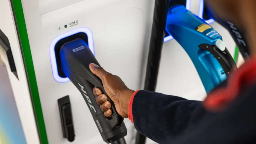 A close up of a man's hand on a EV charging plug. He is placing it back in its holder.