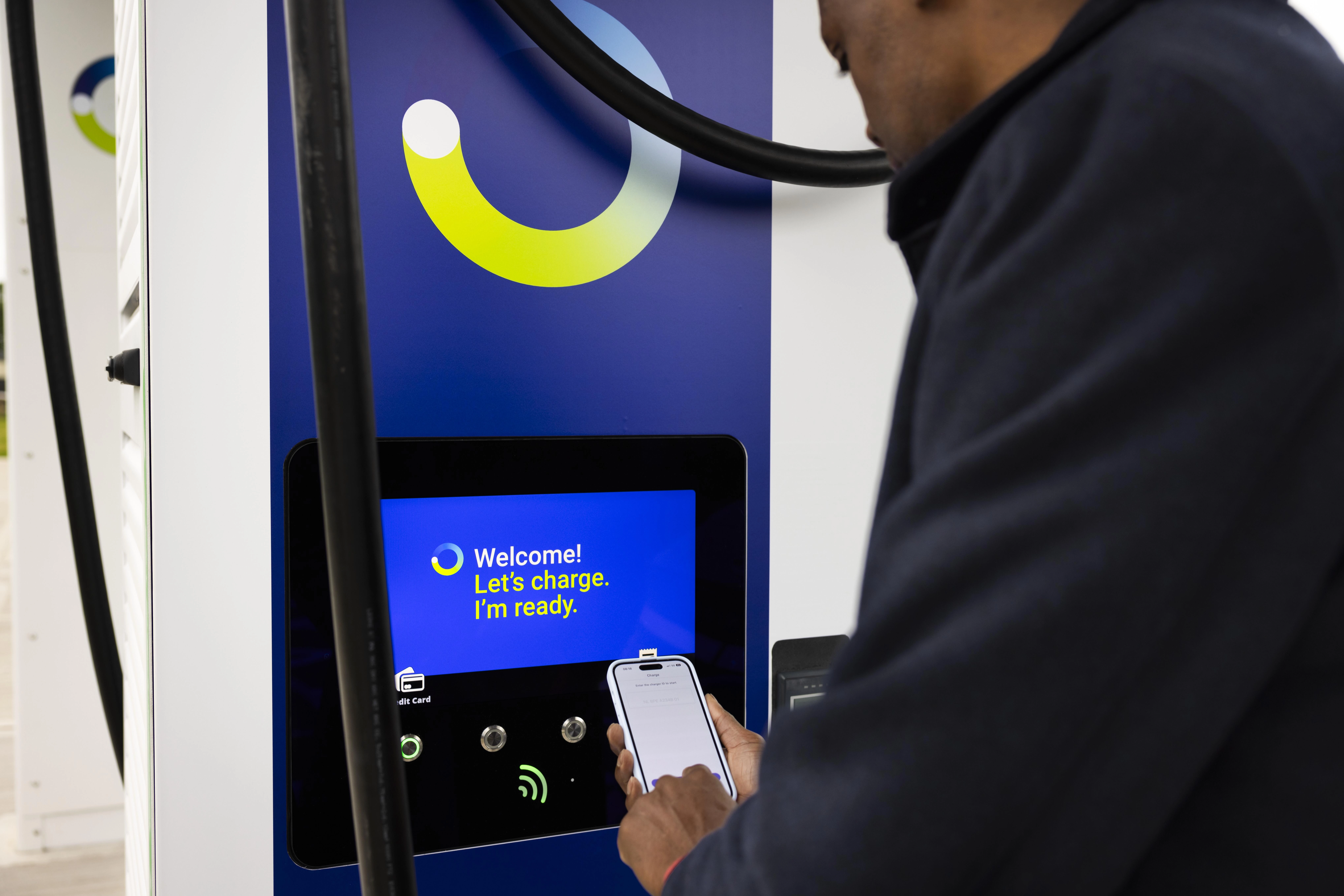 A man holds his phone, which has the bp pulse app open, to a bp pulse ev charger.