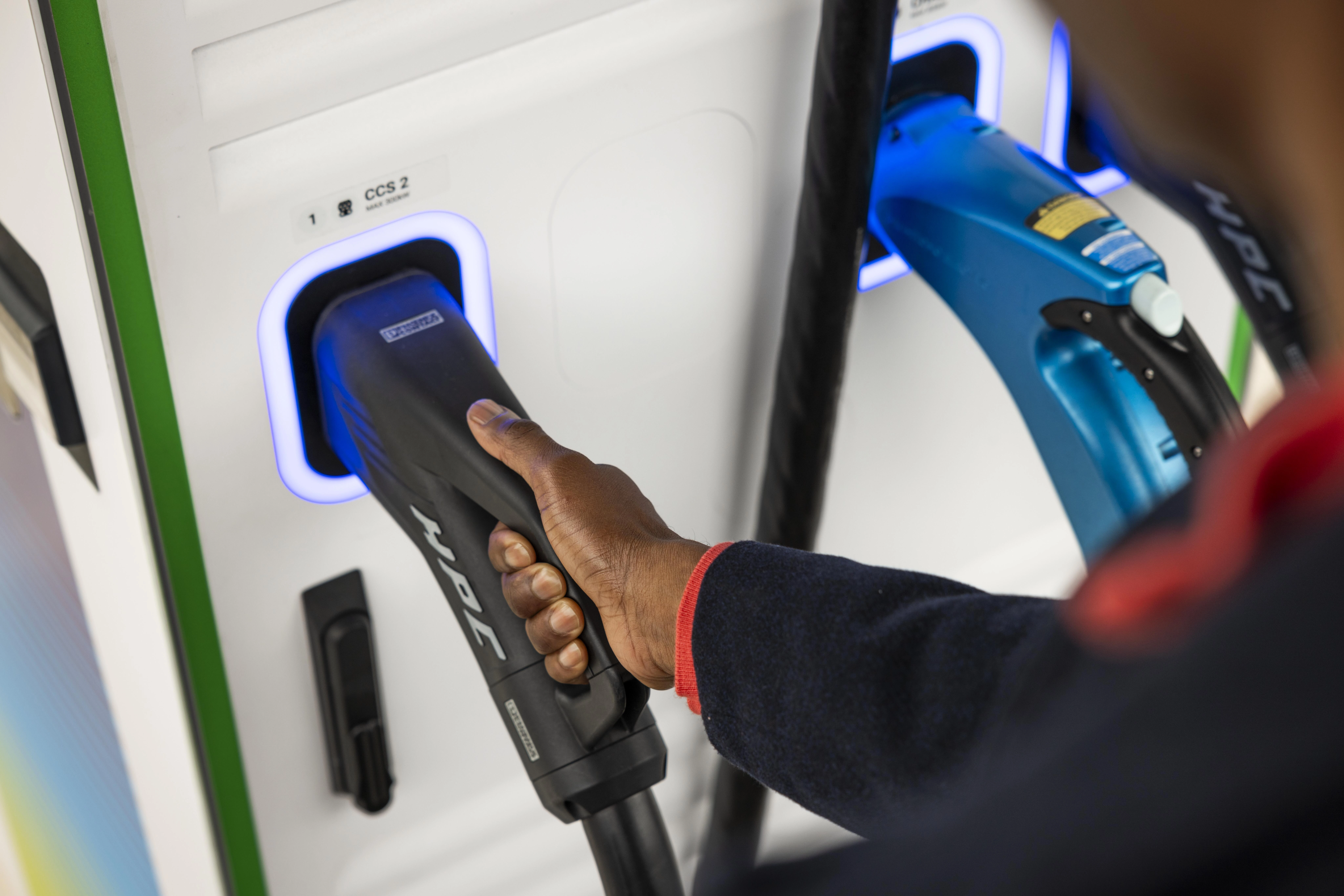 A hand holds the end of a charging cable, ready to connect their vehicle to a bp pulse EV charger.