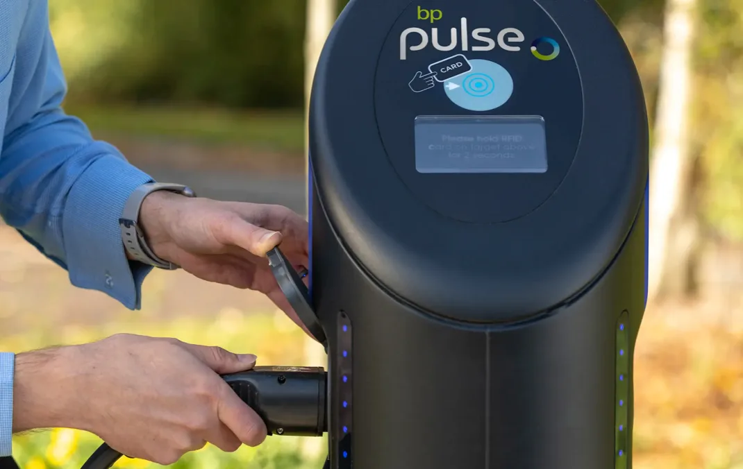 A person is plugging a charging lead into a bp pulse 7kW charging point. Only the hands of the person and the interface of the charging point is visible.