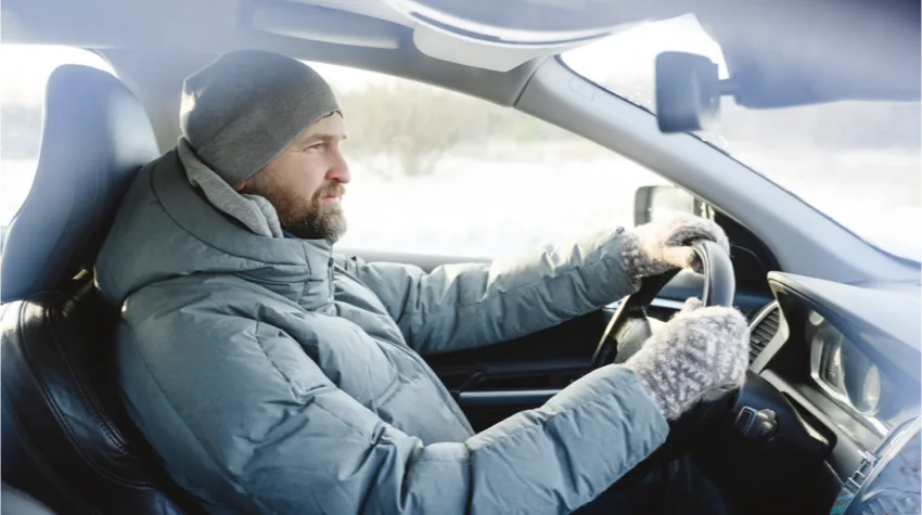 Man dressed in winter gear driving a car.