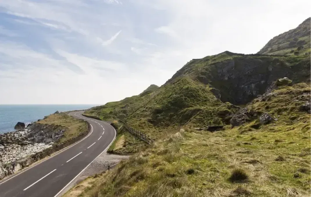 A winding road around the coast, and up a mountain, surrounded by greenery. 