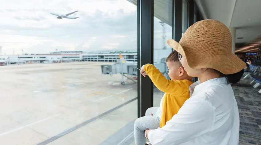 A mother holding her little child boy looking airplane.