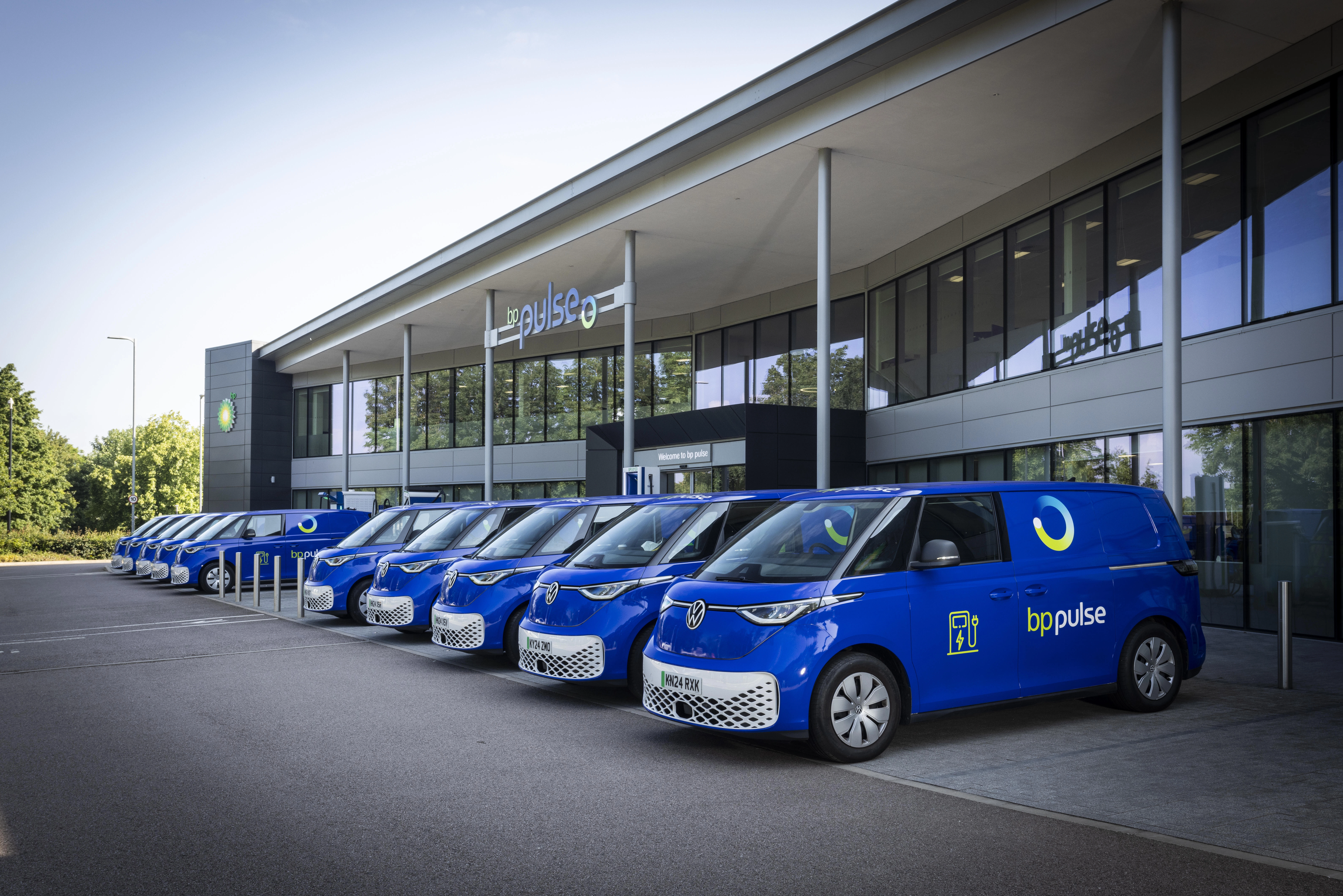 A row of electric vans are lined up outside an office building.