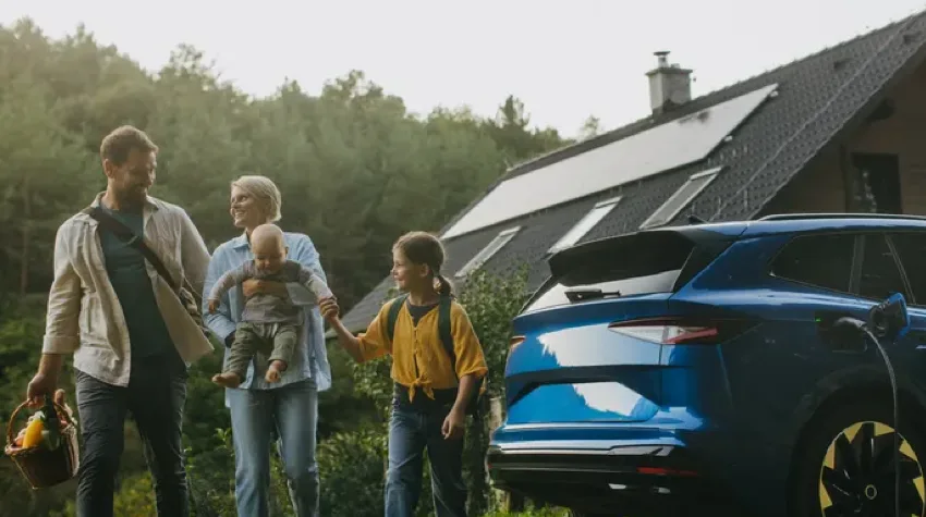 Parents with their two children, smiling and walking, next to a blue car parked outside a house.