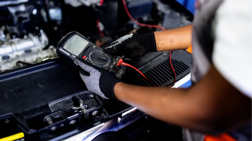 A man carrying out maintenance checks on an Electric Vehicle. He is holding a device connected to the engine with a red wire.
