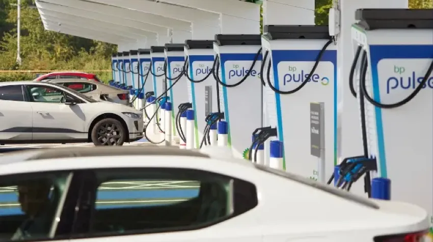 Multiple Electric vehicles are being charged, in a row of charging bays at a bp pulse Charging station. The vehicles are plugged into 150kW chargers and it is a bright clear day.