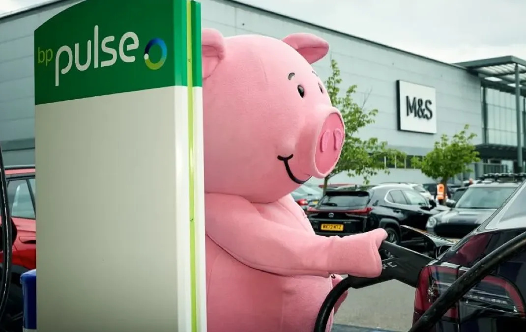 Percy pig plugs his electric vehicle into a bp pulse charger, outside an M&S store.