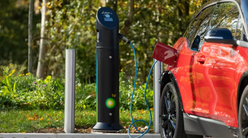 A red EV is charging at a charging point on a sunny day.