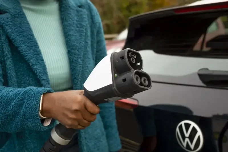A photo of a woman's hand at a bp pulse forecourt, she is holding a charging cable ready to plug in her car.
