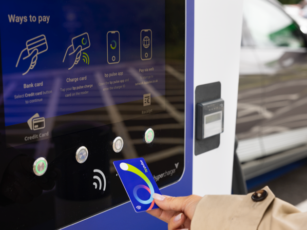 A close up of a woman holding a bp pulse charge card close to a bp pulse EV charger screen. The screen reads 'Ways to pay'.