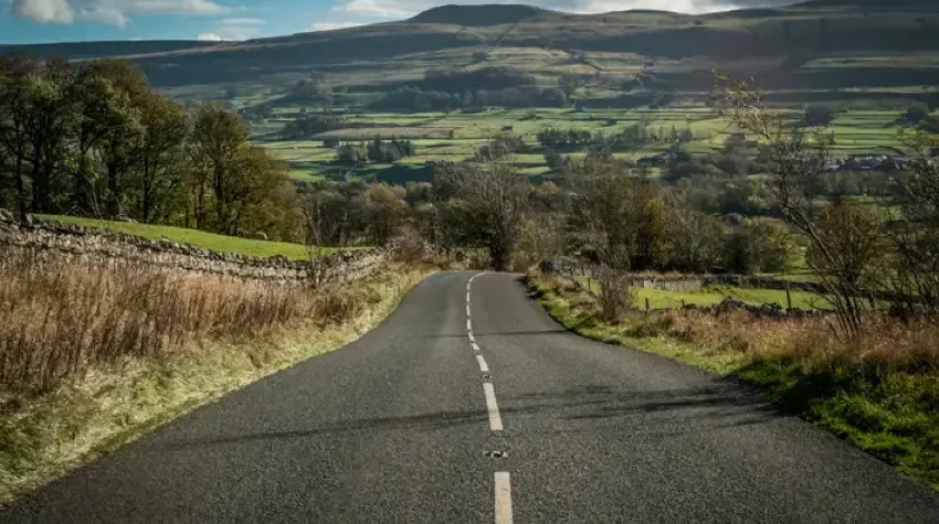 An empty road on a bright day leading to green pastures in the background.
