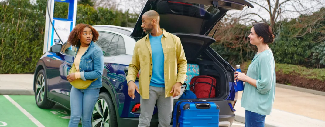 Two women and a man are packing up their EV, ready to go on a trip with their suitcases. 