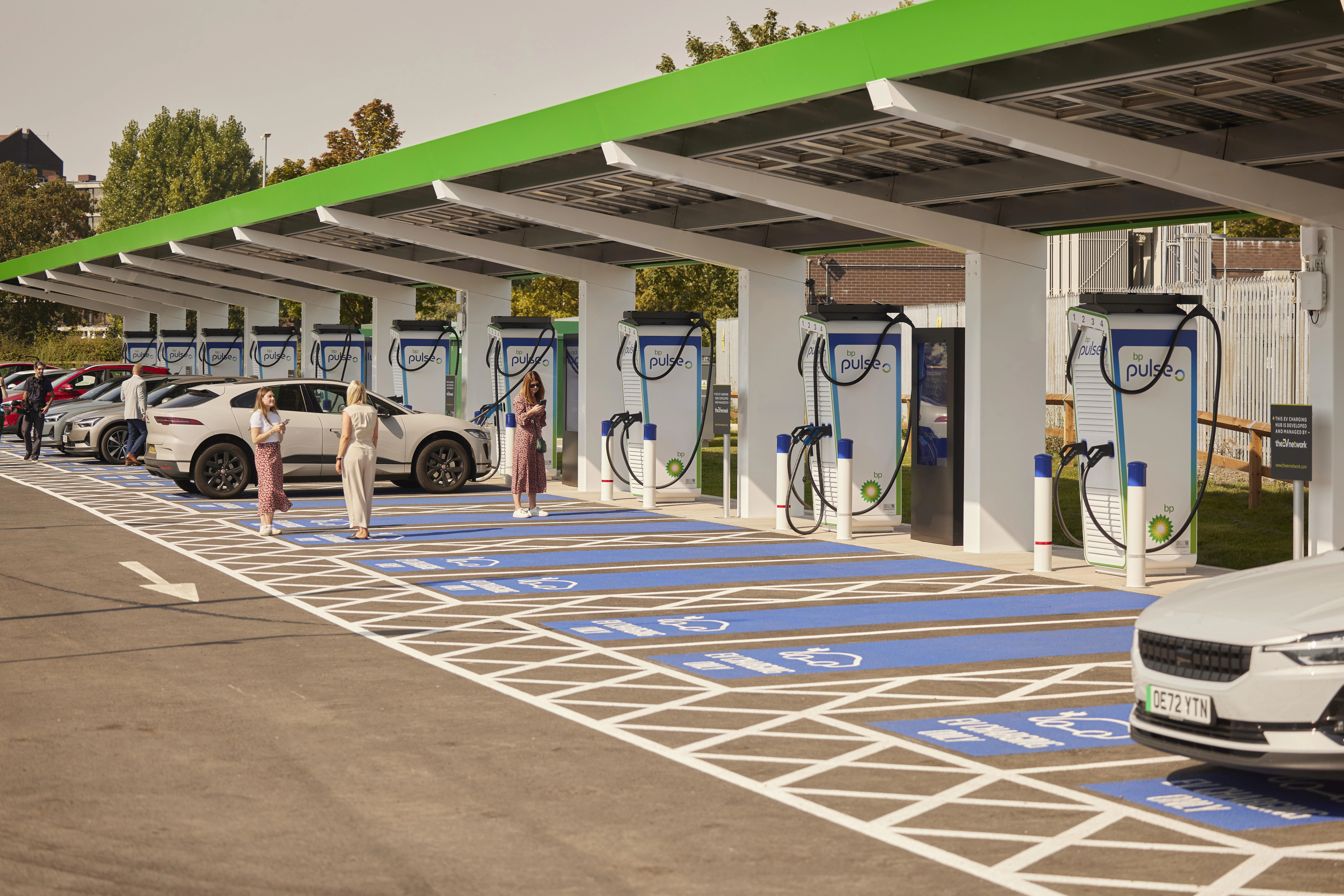 A group of people mingle whilst their electric cars charge at a bp pulse charging site.