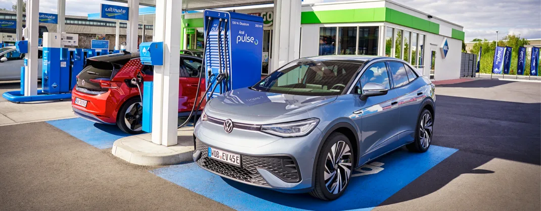 A silver EV charging next to a red EV in a charging station. 