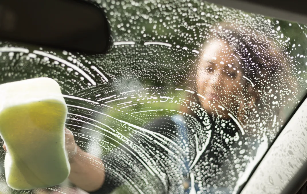 A woman cleans her windscreen with a soapy sponge. 