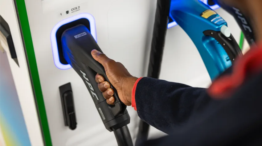 A man holding an electric vehicle charger that is plugged into the station.