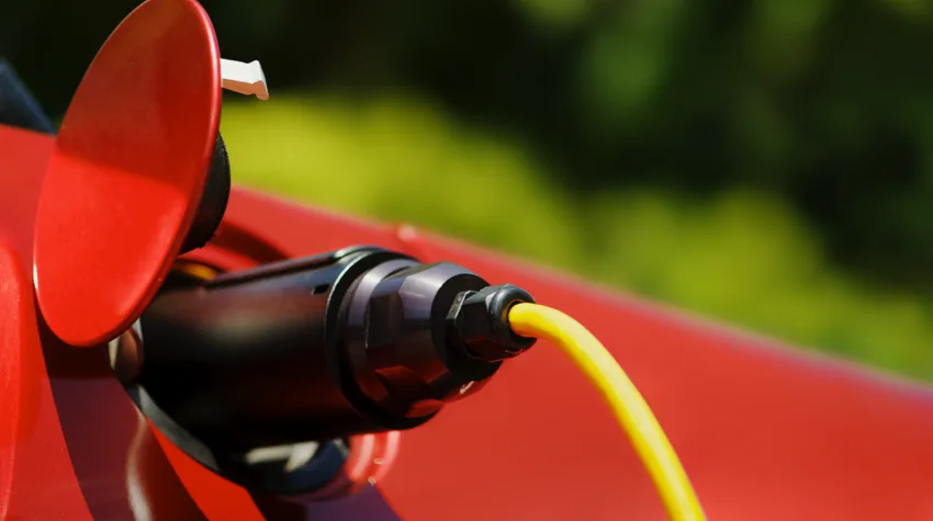 A charger plugged into a red electric car on a sunny day.