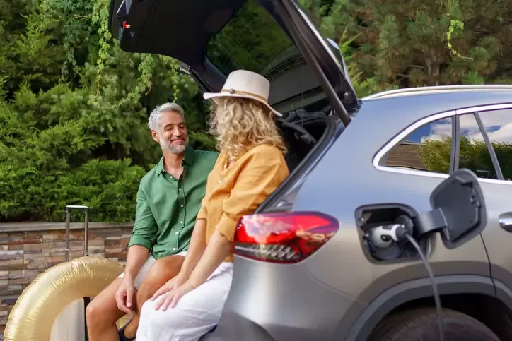 A man and woman sit chatting in the open boot of their electric vehicle whilst it charges.