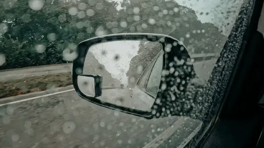 A black wing mirror through a rainy window, on a wet day. 