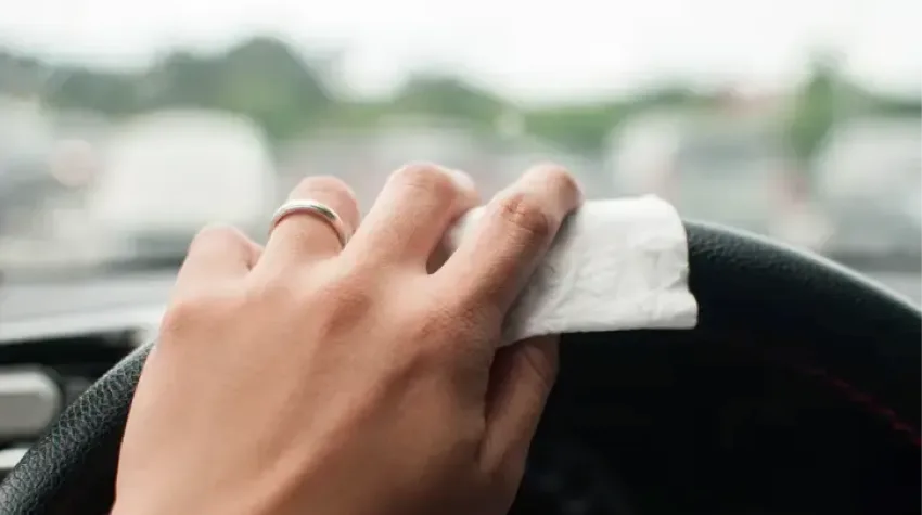 A woman's hand cleaning a steering wheel with a wet wipe. 