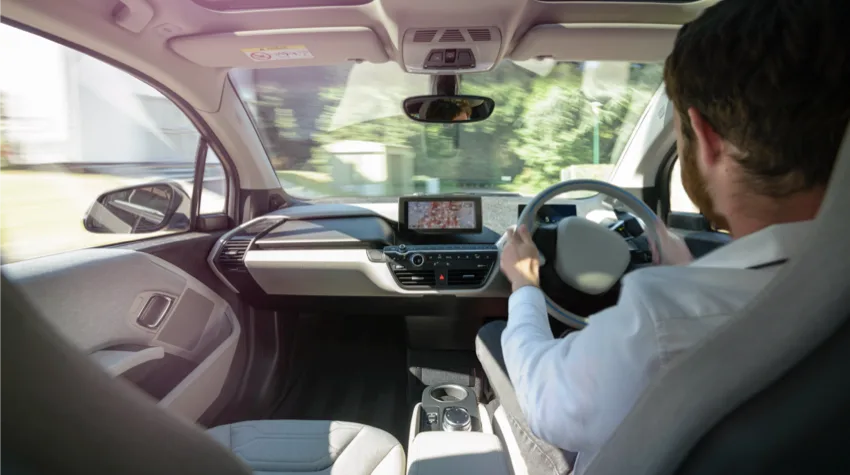 A view from backseat of a car, of man driving the car, on a sunny day.