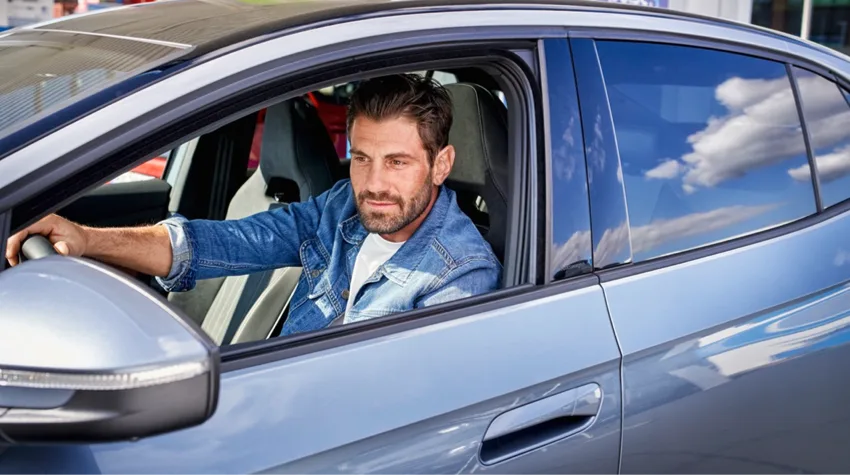 A man driving off in an electric car on a sunny day.